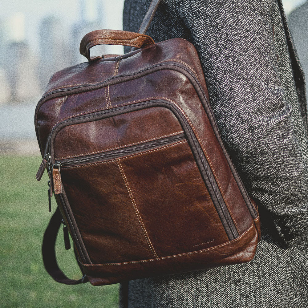 Brown leather backpack held by a person with a blurred background