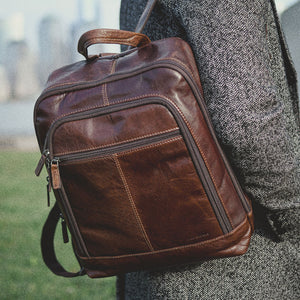 Brown leather backpack held by a person with a blurred background