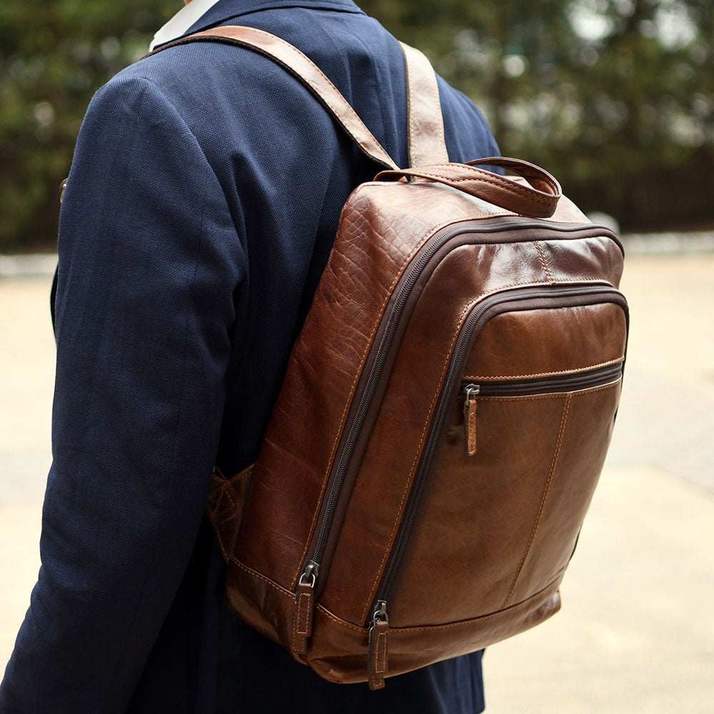 Brown leather backpack worn by a person with a blurred natural background