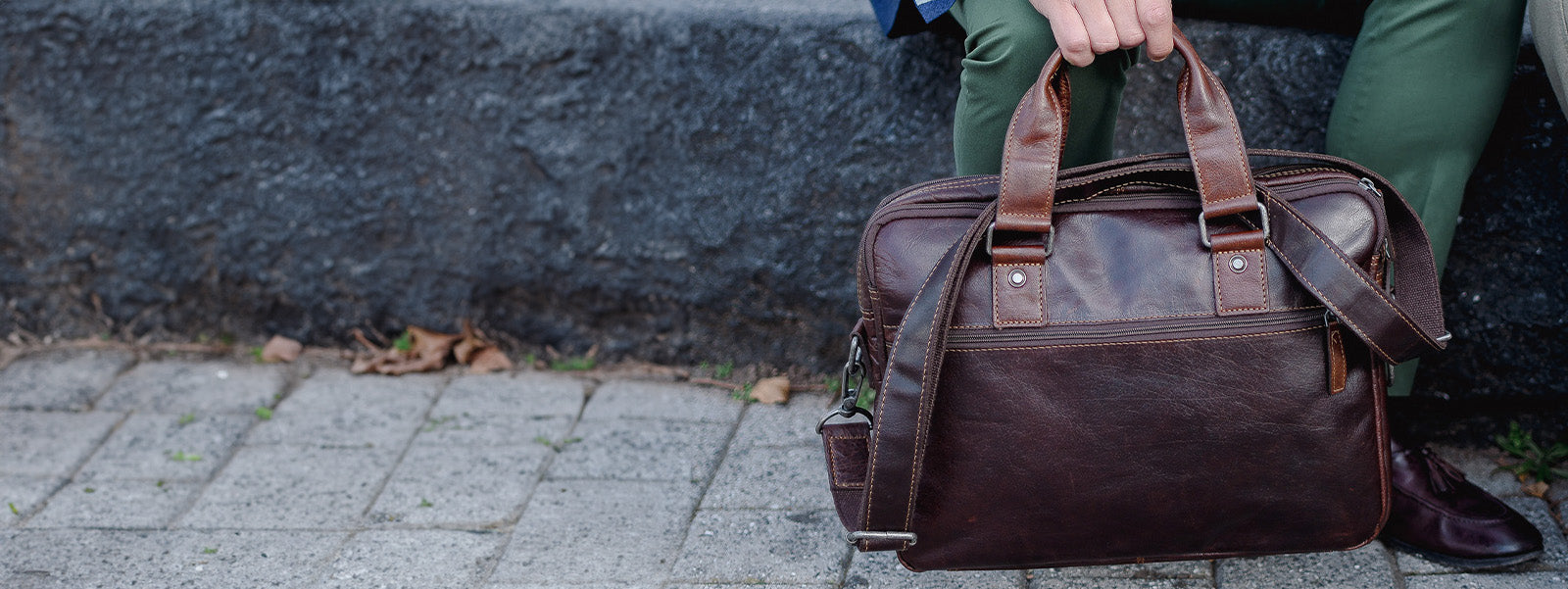 Brown leather briefcase held by a person on a sidewalk.